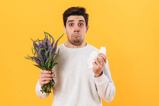 Photo of handsome unhappy man with allergy posing with flowers isolated over yellow background - Φωτογραφία, εικόνα