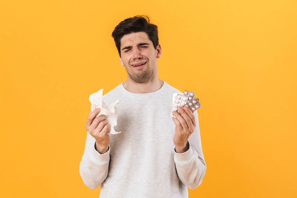 Photo of bristle unhappy man with allergy posing with pills and napkin isolated over yellow background - 写真・画像