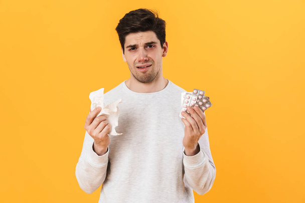 Photo of bristle unhappy man with allergy posing with pills and napkin isolated over yellow background - Photo, Image