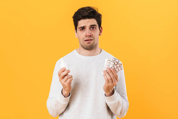 Photo of bristle unhappy man with allergy posing with pills and nose drops isolated over yellow background - Foto, Imagen