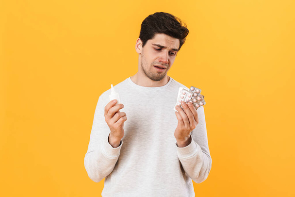 Photo of bristle unhappy man with allergy posing with pills and nose drops isolated over yellow background - Zdjęcie, obraz
