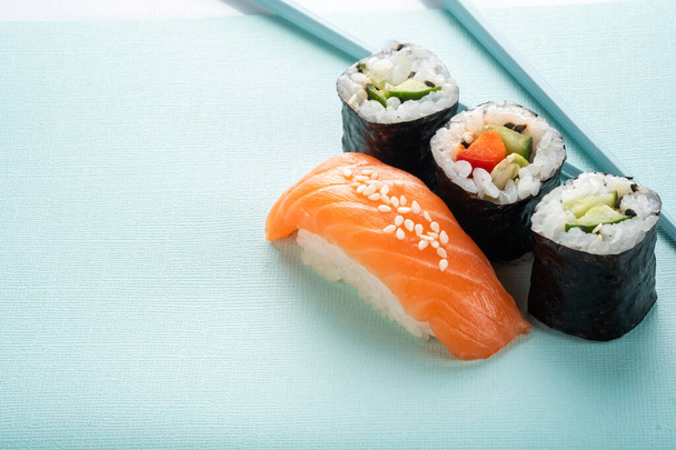 Sushi-Set mit Lachsnigiri und Rolle mit Gurken und Gemüse mit Stäbchen auf blauem Hintergrund, für das Menü der Sushi-Bar - Foto, Bild