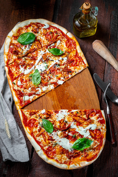 Een lange grote pizza Margarita met zongedroogde tomaten en Basilicum op een houten bord zonder één stuk. Italiaanse keuken rustieke stijl - Foto, afbeelding