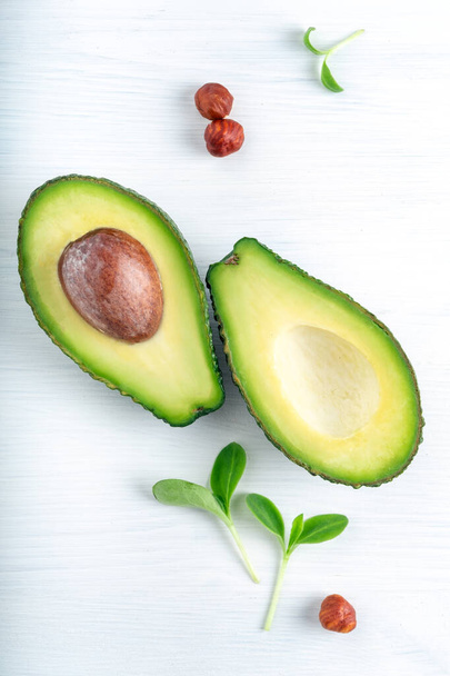 Ripe avocado cut into two parts on a white wooden background with nuts and leaves, one part with a bone. - Foto, immagini