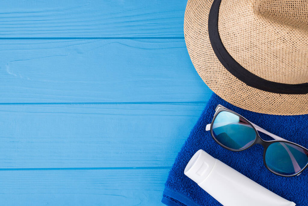 Summertime vacation time concept. Top above overhead view close-up photo of towel sunglasses sunhat and sunscreen isolated on blue wooden background with copyspace - Photo, Image