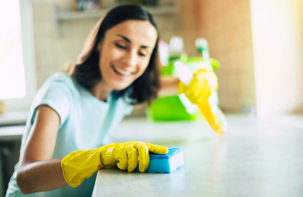 Happy beautiful young woman in yellow gloves is cleaning the kitchen with special equipment and spray. Housework and cleaning stuff - Fotoğraf, Görsel