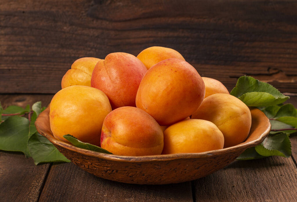 Frische reife Pfirsiche mit Blättern in einer Schüssel auf einem Holztisch. - Foto, Bild