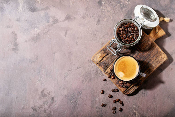 Fresh coffee in glass cup with sugar and coffee beans over brown wooden background. Top view, flat lay - Foto, afbeelding