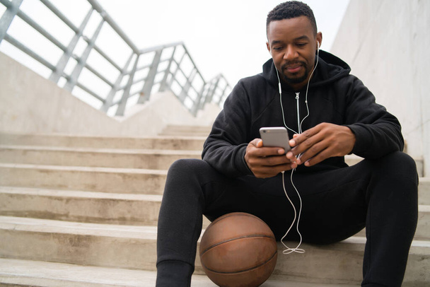 Portrait of an athletic man using his mobile phone on a break from training while sitting on concrete stairs. Sport and health concept. - Foto, Imagem