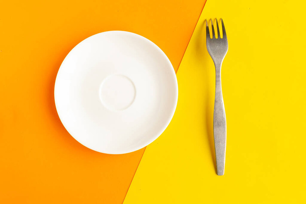 Plaque et fourchette vides sur fond géométrique orange et jaune. Espace de copie pour le texte. Concept minimal - Photo, image