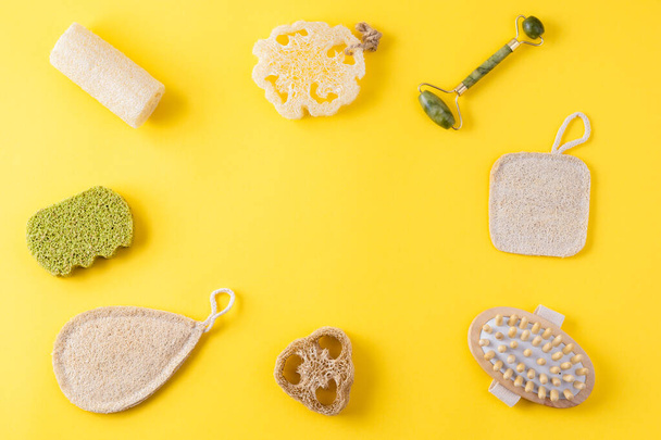 Jade face roller, anti cellulite massager, loofah and bamboo sponges on yellow surface. Frame from tools for beauty routine from ecological material. Zero waste bathroom. Copy space, flat lay - Foto, Imagem