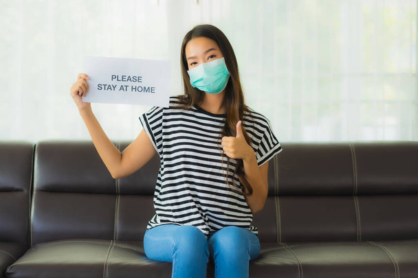 Portrait beautiful young with mask show paper stay home on sofa in livingroom for save people from coronavirus or covid19 - Fotoğraf, Görsel