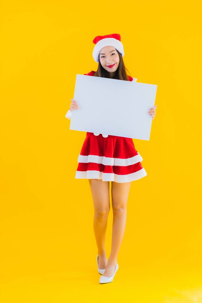 Muotokuva kaunis nuori aasialainen nainen jouluvaatteet ja hattu hymy tyhjä valkoinen aluksella merkki keltainen eristetty tausta
 - Valokuva, kuva