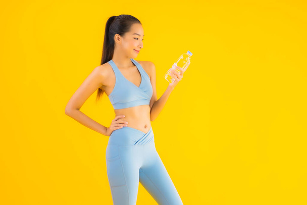 Ritratto bella giovane donna asiatica con bottiglia d'acqua su sfondo giallo isolato - Foto, immagini