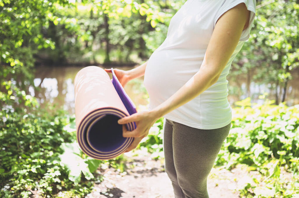 Unrecognizable young pregnant woman preparing to do yoga exercising with pink yoga mat. Active future mother sport lifestyle. Healthy pregnancy concept. - Photo, Image