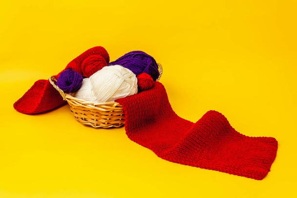 on an orange background, a wicker basket, through which a red knitted scarf is stretched, in the basket skeins of woolen threads of blue and white colors - Foto, Bild