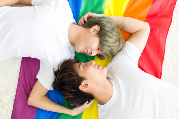 Aziatische mannelijke homoseksuele of homoseksuele stellen liggen op een regenboogvlag, en beiden maken samen oogcontact. Concept van LGBTQ-trots. - Foto, afbeelding
