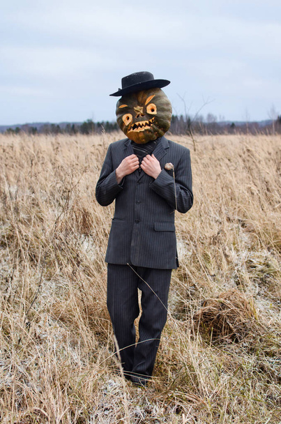 espantalho monstruoso com uma abóbora de Halloween em sua cabeça fica em um campo selvagem vestido com um terno de negócios
 - Foto, Imagem