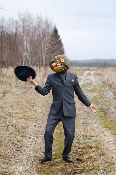 espantalho monstruoso com uma abóbora de Halloween em sua cabeça mostra e dança em uma estrada rural vestida com um terno de negócios
 - Foto, Imagem