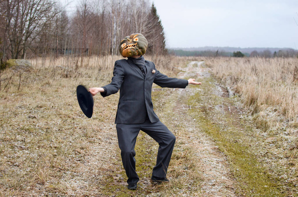 mostruoso Spaventapasseri con una zucca di Halloween in testa si esibisce e balla su una strada di campagna vestita con un abito da lavoro - Foto, immagini