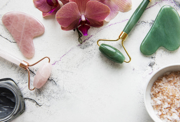 Набор натуральных органических спа-косметики с цветами орхидеи. Плоская соль для ванн, ролики для лица, цветы орхидеи на мраморном фоне. Уход за кожей, концепция косметики - Фото, изображение