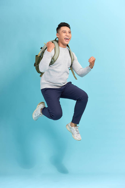 Szczęśliwy młody atrakcyjny mężczyzna skacze i macha ręką, nosząc podstawowe ubrania z plecakiem - Zdjęcie, obraz