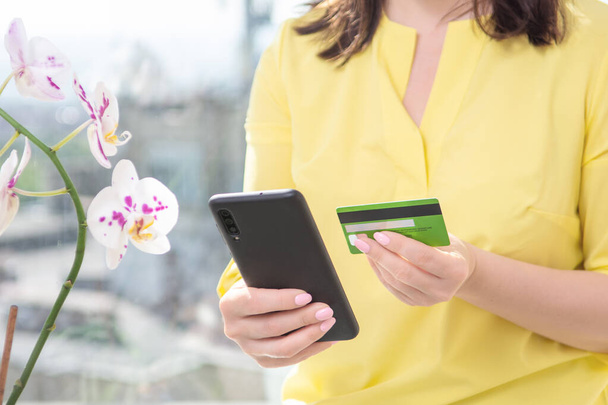 Young woman making online payment with credit card and smartphone. Woman shopping online with credit card using cell phone at home. Indoor. - Photo, image