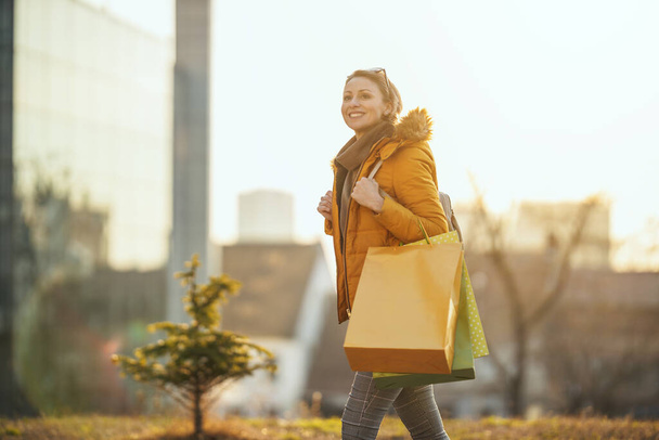Młoda uśmiechnięta kobieta spaceruje po mieście z torbami na zakupy. - Zdjęcie, obraz