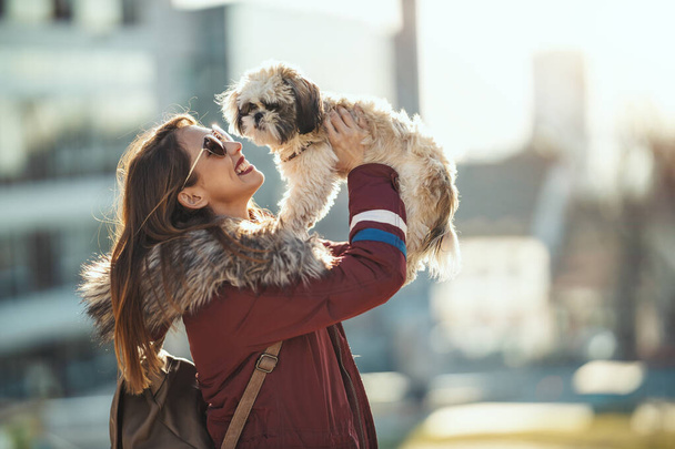 Όμορφη νεαρή γυναίκα μόδας ξοδεύει χρόνο με χαριτωμένο κατοικίδιο ζώο σκυλί της παίζει στο δρόμο της πόλης.  - Φωτογραφία, εικόνα