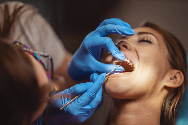 Die schöne junge Frau ist beim Zahnarzt. Sie sitzt auf dem Zahnarztstuhl und der Zahnarzt setzt sich Zahnspangen auf die Zähne und legt ästhetisch selbstausrichtende Lingualschlösser an.. - Foto, Bild