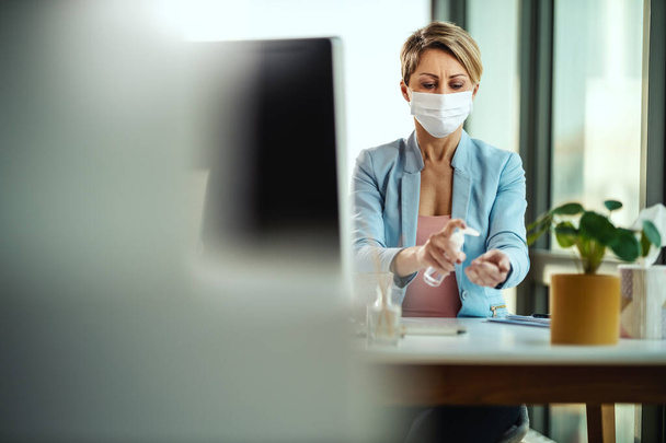 医療用保護マスクのビジネス女性は、手の消毒のための抗菌防腐ゲルを使用し、インフルエンザウイルス感染症やコロナウイルスの流行中に感染を避けるために、自己分離と隔離中にコンピュータで自宅から動作します。. - 写真・画像