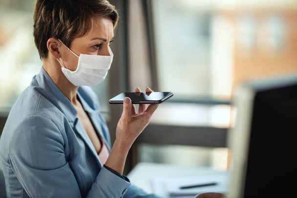 Business woman in a medical protective mask works at the computer and talking on a smartphone during self-isolation and quarantine to avoid infection during flu virus outbreak and coronavirus epidemic - Photo, Image