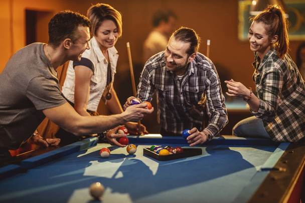 Jonge vrolijke vrienden spelen biljart in de bar na het werk. Een koppel dat roem wint en de verliezers zijn in een slechte bui.. - Foto, afbeelding
