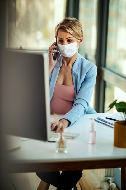 La mujer de negocios con una máscara de protección médica trabaja en la computadora y habla en un teléfono inteligente durante el autoaislamiento y la cuarentena para evitar la infección durante el brote del virus de la gripe y la epidemia de coronavirus.
. - Foto, imagen