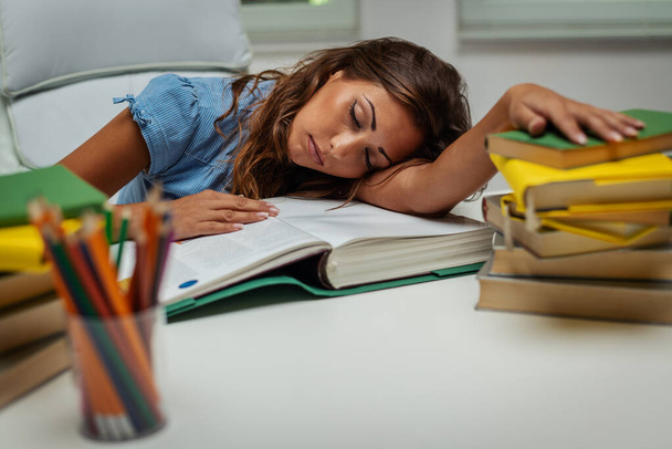 A beautiful tired young female student is sleeping on the books while preparing exam and learning lessons in school library. - Фото, изображение