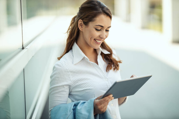 Jeune femme d'affaires souriante surfe sur les réseaux sociaux sur une tablette numérique devant le bureau pendant la pause. - Photo, image