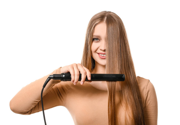 Beautiful young woman using flattening iron for hair against white background - 写真・画像