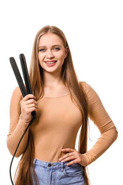 Beautiful young woman with flattening iron for hair against white background - Photo, Image