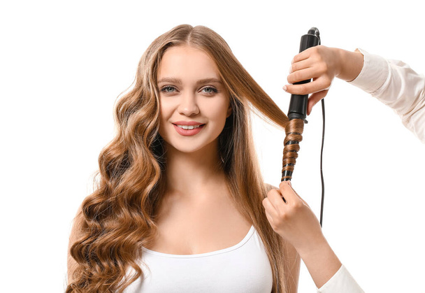 Hairdresser curling hair of beautiful young woman against white background - Foto, Bild
