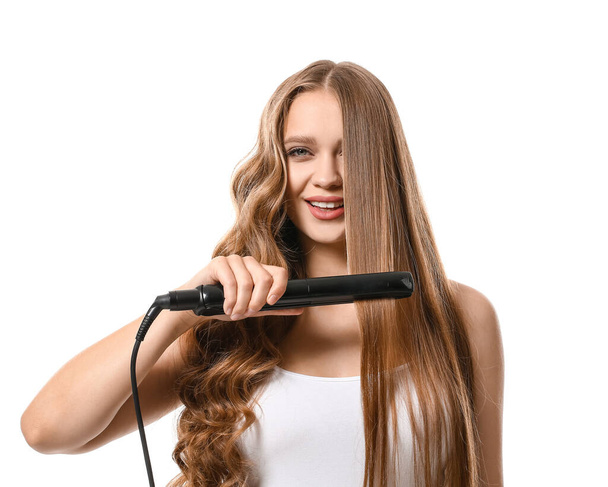 Beautiful young woman with flattening iron for hair against white background - Foto, imagen