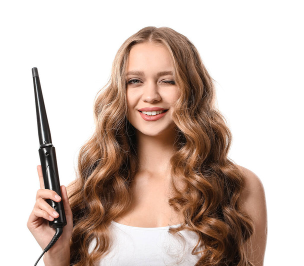 Beautiful young woman with curling iron for hair against white background - Photo, image