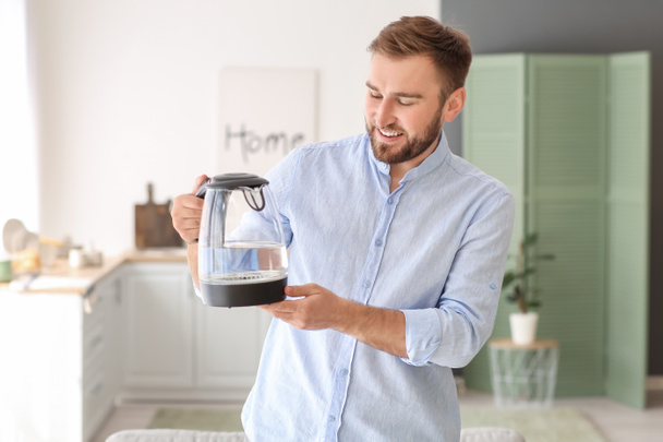 Young man with electric kettle at home - Valokuva, kuva