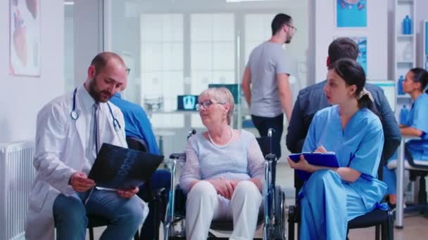Medico titolare di radiografia della donna anziana disabile sulla sedia a rotelle - Filmati, video