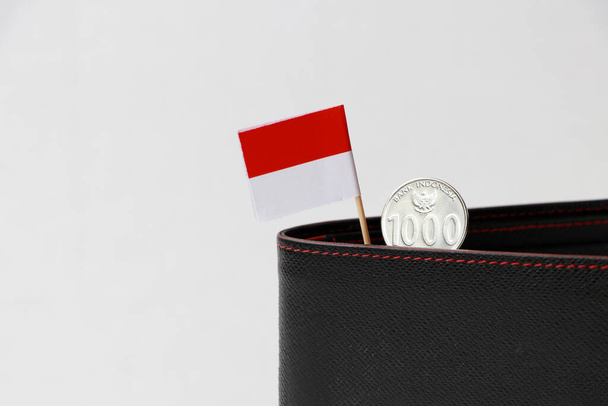 Ezer Rupiah mini Indonézia zászlórúddal a fekete pénztárcán, fehér háttérrel. A finanszírozás vagy a pénznem fogalma. - Fotó, kép