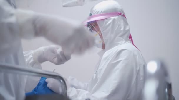 Dentysta i jego personel pielęgniarski pracujący nad pacjentem leżącym z okryciem na twarzy podczas operacji jamy ustnej w klinice stomatologicznej, maska ochronna garnituru Papieża, ochrona przed wirusami covid-19 - Materiał filmowy, wideo