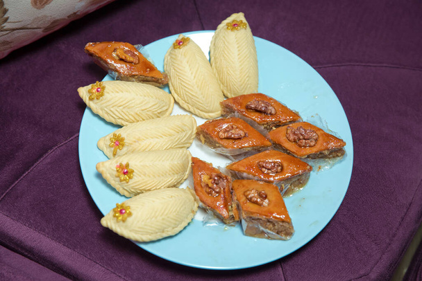 Baklava and Shekerbura on a plate. Shekerbura with nuts and honey. Baklava and Shekerbura blue plate purple background . - Photo, Image