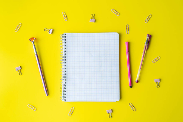 School supplies and a notebook lie on a yellow background. In the center, on a yellow surface, is a notebook, a place to copy space. Stationery, paper clips, post-it notes. Back to school. - Foto, Imagen