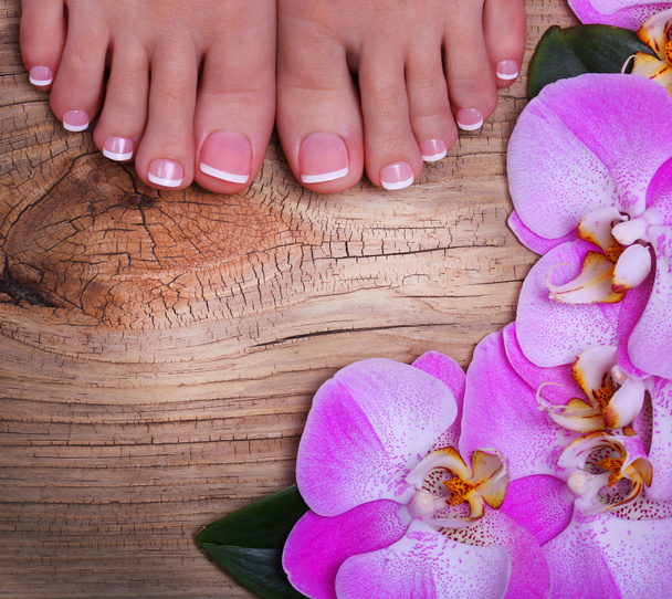 Pedicure with pink orchid flowers on wooden background. - Photo, Image