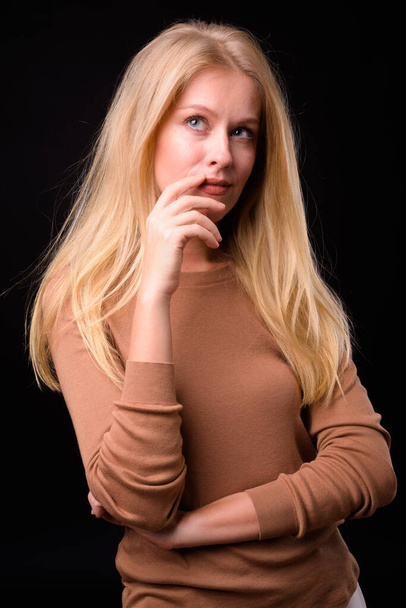Студийный снимок красивой женщины со светлыми волосами в свитере на черном фоне - Фото, изображение