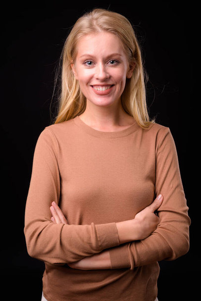 Studio shot of beautiful woman with blond hair wearing sweater against black background - Zdjęcie, obraz